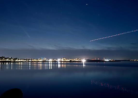 seaside scene with a comet being photobombed by the flashing red lights of an aeroplane incoming from the right