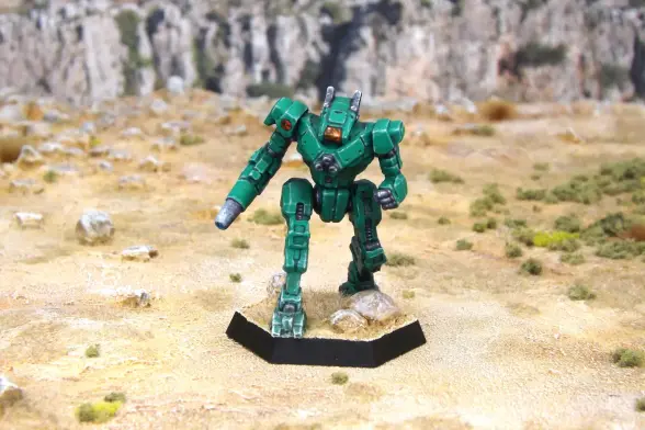 A painted miniature of a Wolfhound 'Mech.  It is emerald green and the cockpit glass is orange.  The emblem of Wolf's Dragoons is on the right shoulder.  The greek letter beta is just visible on the left leg.  The miniature is photographed on rocky terrain.