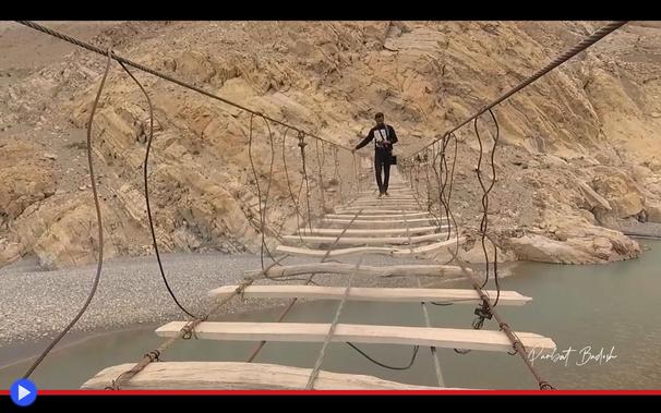 Veduta prospettica di un ponte sospeso costruito in legno e corde, in cui circa la metà delle traversine sono assenti. Una figura umana, sulla distanza, appare in posizione precaria mentre si appresta ad attraversarlo.