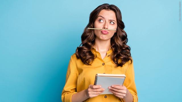 Junge Frau hat einen Stift zwischen Lippen und Nase und zieht denkend die Augenbraue hoch. Symbolbild für: Apostroph im Deutschen? Wann wird es gesetzt? Tipps zur Rechtschreibung. (Foto: Adobe Stock, deagreez)