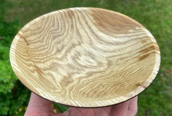 An oak bowl, resting on finger tips, showing just the inside, tan and  brown, streaked with grain patterns.