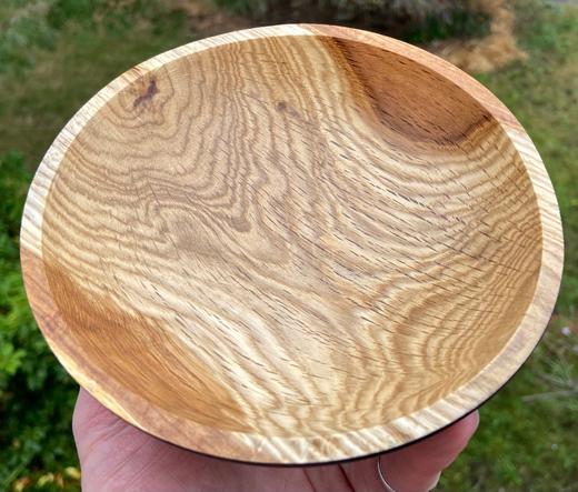 A second oak bowl, resting on finger tips, showing just the inside, tan and  brown, streaked with grain patterns.