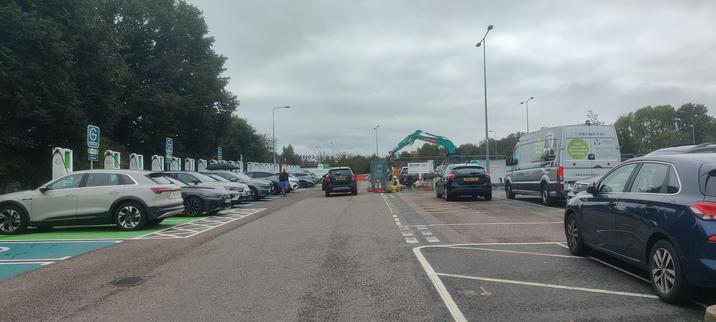 A line of 21 chargers, each with an electric vehicle leading into the distance where a crane and construction workers are seen laying the infrastructure for more chargers.