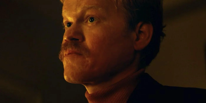 Jesse Plemons looks intently over his bushy yet tidy moustache, wearing a turtleneck jumper and jacket, in the movie Kinds of Kindness