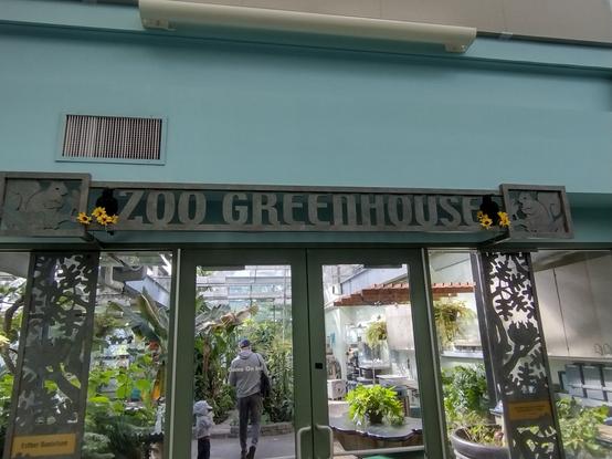 The entrance to Brookfield Zoo's greenhouse. It features an intricate antique style metal sign reading "Zoo Greenhouse," accented with seasonal decorations of ravens and flowers for autumn.