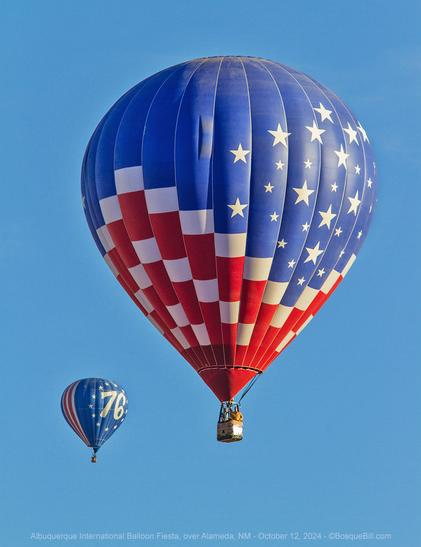Two hot air balloons against a clear blue sky. The larger in the middle is blue on top with white stars and checker board red & white stripes below; the second farther away, so smaller, in the bottom left is half blue with "76" in white surrounded by a circle of stars; the back half are vertical red and white stripes.
©BosqueBill.com