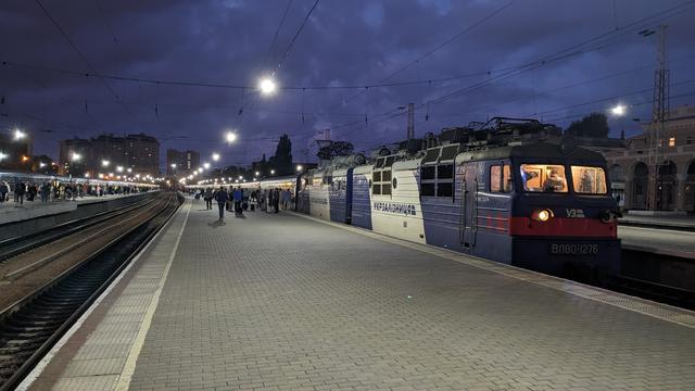 A UZ VL 80 locomotive with a long passenger train at a broad gauge station with real platforms.