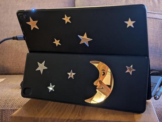 The back of a black laptop/tablet case decorated with a number of gold shiny stars and a gold smiling half moon face.