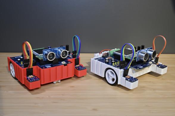 Two 3D-printed BEAPER Pico robots controlled by Raspberry Pi Pico microcontrollers. Both have optical floor sensors and SONAR modules to sense their environment.