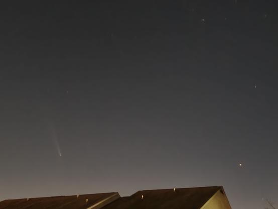 Comet Tsuchinshan-ATLAS on the left, with a long tail, in a grey dark sky above a building. The bright star on the right corner is Arcturus.