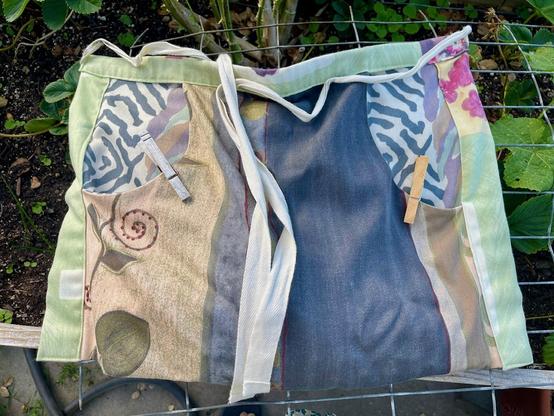 A clothespin apron is spread out over the wire of our strawberry bed. One pocket opening has a well-used clothespin clipped to it; the other pocket has a new clothespin.