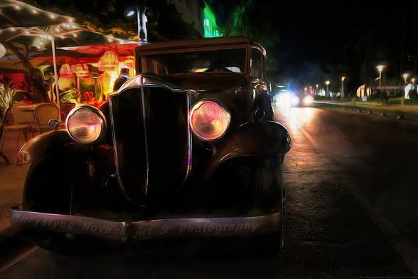 A vintage Packard automobile with glowing headlights is parked on a street at night, giving off a classic vibe amidst the modern surroundings. The photo painting has a dreamy quality, highlighting the car's sleek lines against a backdrop of ambient street lights and a night-time atmosphere.
