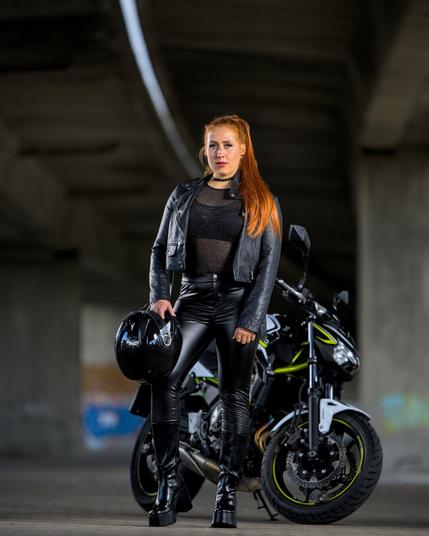 read haired girl in leather clothes standing in front of a kawasaki motorcycle.
