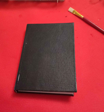 Hardcover Book, with black faux leather cover view from above, on top of a red tablecloth.