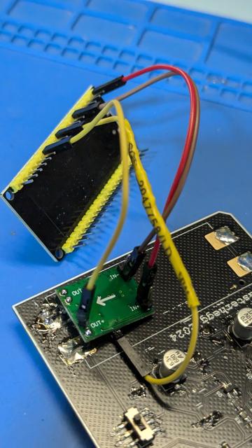 the backside of the Easterhegg 2024 badge with the battery pack desoldered. In it's stead, a step-down converter is soldered on. The step-down is connected to an ESP32 devkit board.