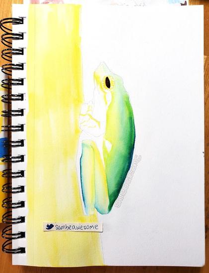 A photo of a sketchbook with a lightly drawn pencil sketch of a tree frog seen from the side, legs and arms tucked under its body. A light yellow takes up the left half of the page and the frog is gradually being filled in with greens and yellows.