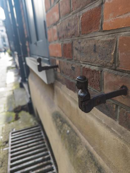 Next to closed wooden shutter are moveable metal holder in the shape of a human head and shoulders that could be used to hold it open.