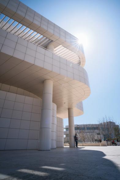 A curved building with square tiles. A man leaning against a pillar. Sunstar.