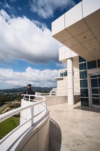 A curved building with square tiles. A man leaning against a railing. Cloudy skies but sunny