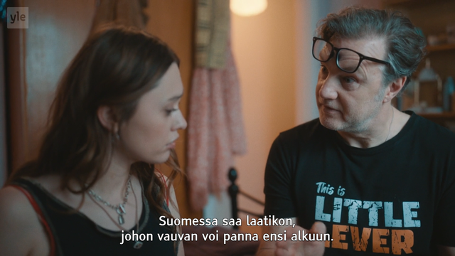 Kuvakaappaus sarjasta, jossa silmälaseja otsallaan pitävä isä kertoo tyttärelleen, että Suomessa saa laatikon, johon vauvan voi panna ensi alkuun.