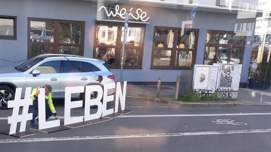 #LEBEN Schriftzug aus ca. 1 m hohen Buchstaben auf dem Radfahrstreifen vorm Café Weise in Düsseldorf-Wehrhahn.

Quelle: https://www.reddit.com/r/duesseldorf/comments/1g4wbkn/leben_und_damit_den_radstreifen_blockieren_das/
