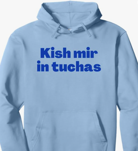 The Yiddish curse Kish mir in tuchas is shown in blue lettering on a light blue hoodie.