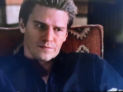 Angel (actor David Boreanaz) in a chair with a pattern in his office at Angel Investigations. His head is slightly tilted right and his eyes are cast down and to the right. He is wearing a black dress shirt. From Angel Season 1, Episode 22.