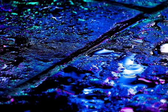 Blue and pink neon lights reflect in puddles of water on a Glasgow street during a heavy rainstorm