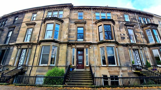 Looking up at a terrace of three-storey blonde sandstone Victorian townhouses.