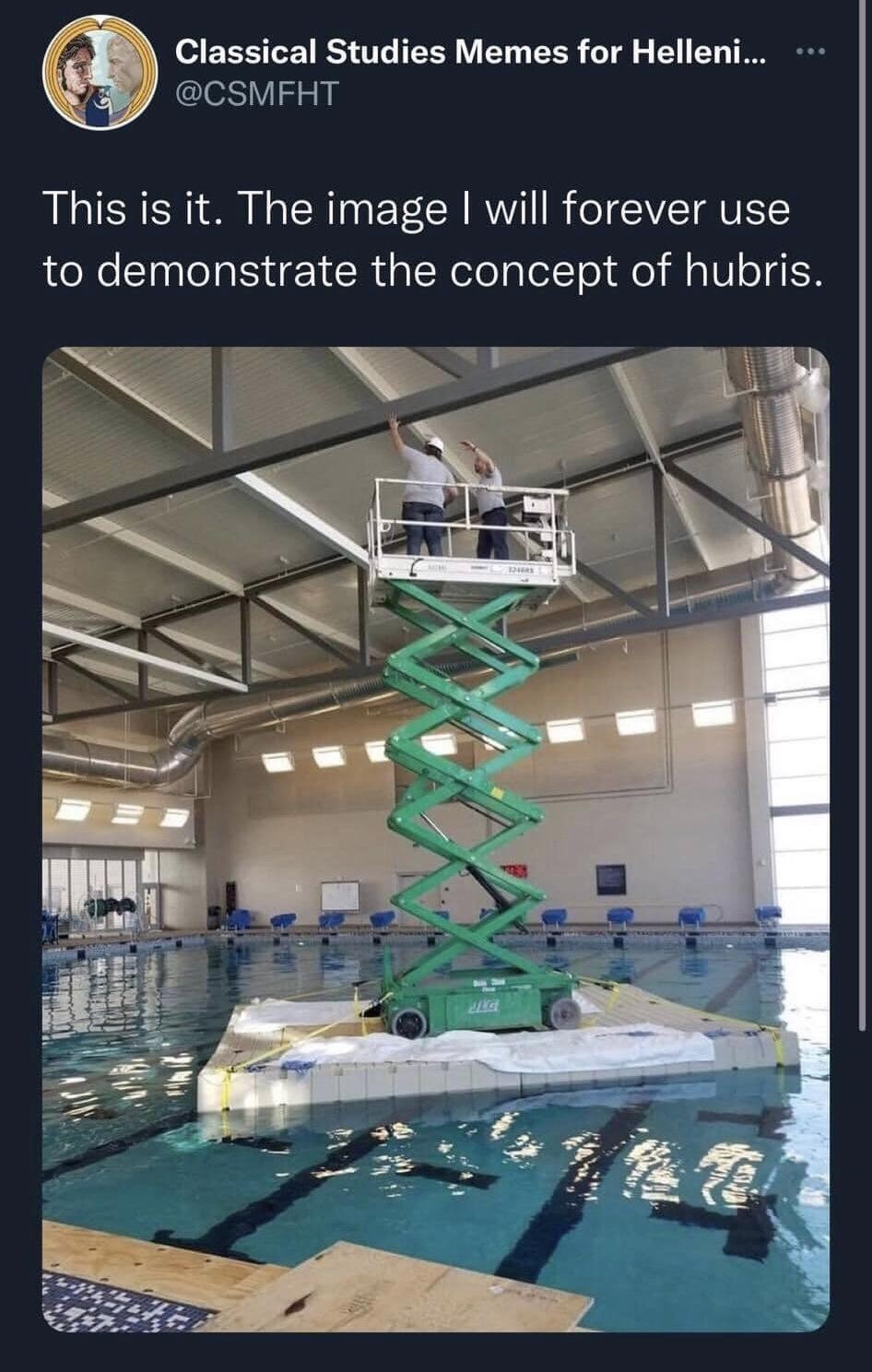 "This is it. The image I will forever use to demonstrate the concept of hubris." Photo of an extended scissor lift on a makeshift raft in the middle of a large, indoor pool. Two workers wearing hardhats can be seen on the lift near the support beams handling some electrical lines.