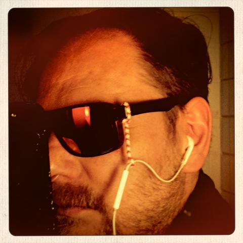 cosmic trägt Sonnenbrille. Das Mikrofon seines weißen, kabelgebundenen Apple Airpods Headsets ist mit einen gebogenen Pfeifenreiniger am Brillenbügel befestigt. Dadurch wird es in der idealen Position gehalten: Relativ nah, aber seitlich vom Mund, um sowohl Plosiv-Laute (Pop, Plop) als auch Nasen-Schnaufgeräusche (Vader) vom Mikro fernzuhalten.
