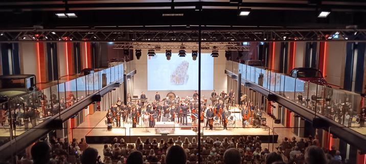 Im Saal des Einbecker PS.Speichers auf der Bühne vor voll bestem Saal ein großes Orchester, stehend beim Schlussapplaus, mit Richie Müller als Vorleser