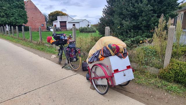 The chrome and red cart stands behind the bike next or the road, there's clearly something wrong as it's leaning forward and isn't attached