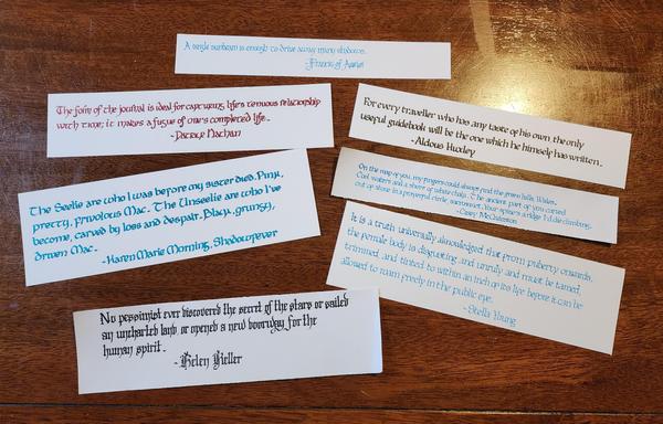 Seven strips of paper, each with a different quote calligraphied on them in different scripts and ink colours. the quotes are:

A single sunbeam is enough to drive away many shadows - Francis of Assisi

Th form of the journal is ideal for capturing life's tenuous relationship with time; it makes a fugue of one's completed life. - Patrick Nathan

The Seelie are who I was before my sister died. Pink, pretty, frivolous Mac. The Unseelie are who I've become, carved by loss and despair. Black, grungy, driven Mac. - Karen Marie Morning, Shadowfever

For every traveller who has any taste of his own, the only useful guidebook will be the one which he himself has written. - Aldous Huxley

On the map of you, my fingers could always find the green hills, Wales. Cool waters and a shore of white chalk. The ancient part of you carved out of stone in a prayerful circle, sacrosanct. Your spine's a ridge I'd die climbing.
- Casey McQuinston

It is a truth universally acknowledged that from puberty onwards, the female body is disgusting and unruly and must be tamed, trimmed, and tinted to within an inch of its life before it can be allowed to roam freely in the public eye. - Stella Young

No pessimist ever discovered the secret of the stars or sailed an uncharted land, or opened a new doorway for the human spirit. - Helen Keller