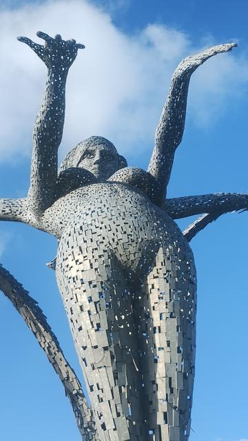 Standing in front of the statue, looking straight up , autumn sunlight on one side of it, blue skies above, closer zoom this time