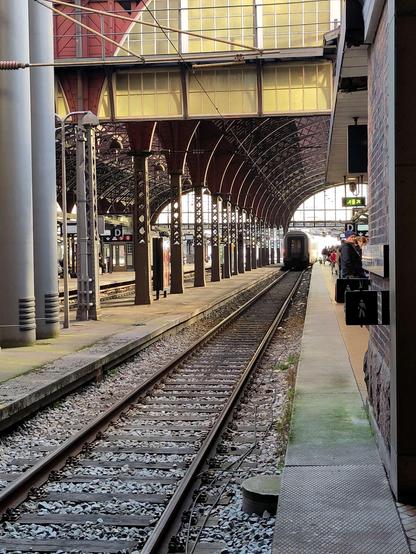 An old diesel locomotive approaches. Platform through curved arches lit by low autumn sun