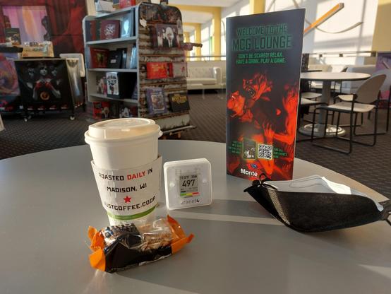 A takeout coffee, a Kind breakfast bar, and an Aranet4 reading 497 ppm CO2.
