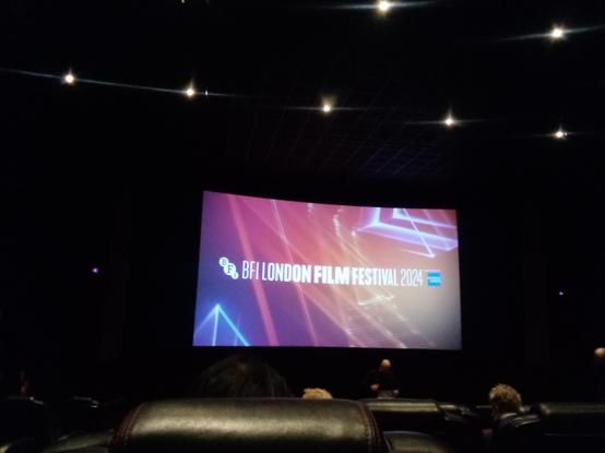 A cinema screen with "BFI London Film Festival 2024" in white text on a pinky purpley orange background. In the foreground you can see the backs of some of the seats in front.
