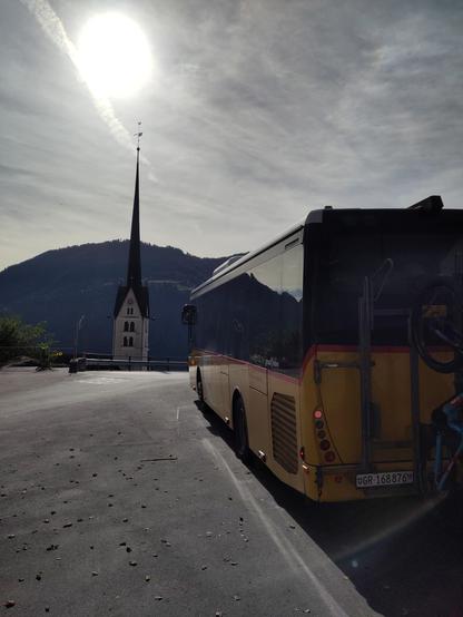 Foto. Ein gelber Bus und ein Kirchturm.