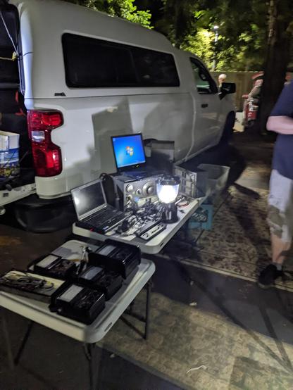 a ham radio operator with their display of items they are selling at the ham swap meet: two thinkpads, an older radio,  multiple voltmeters, and more