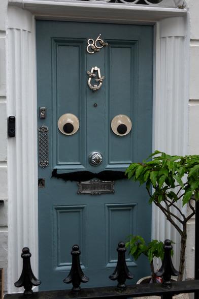A door has two large googley eyes on it, and a wide mustache above the letterbox, creating the appearahce of a face.