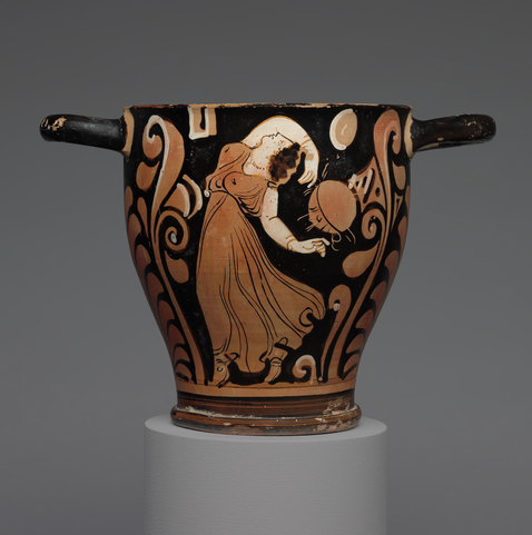 Terracotta cup in orange, white, and black showing a woman (maenad) in ancient dress dancing with her arm above her head.