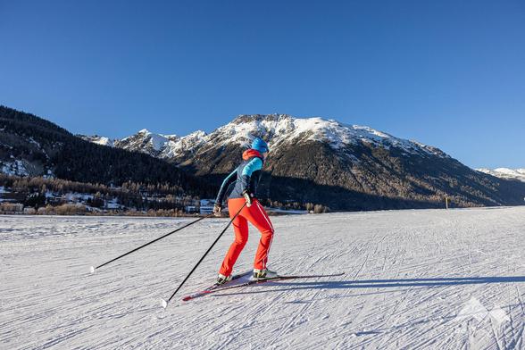 Woman on skating skis on a cross-country ski run, wearing red trousers and a blue jacket.
