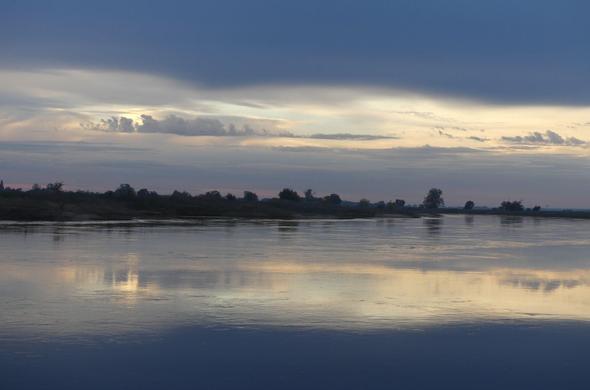 auf einer Buhne in der Elbe stehend Blick nach rechts, Himmel oben dunkelgrau, darunter bühnenartig eine Lücke mit leuchtenden Wolken und Licht, alles spiegelt sich in der Elbe, kein Vogel weit und breit