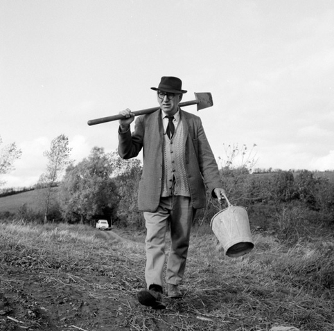 Patrick Kavanagh in a field with a bucket and a sleán, a turf cutting spade, over his shoulder.
