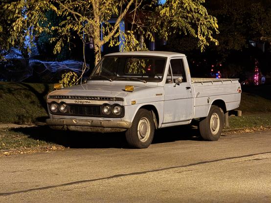 A first generation (1968-1972) Toyota HiLux pickup truck parked on the street at night.