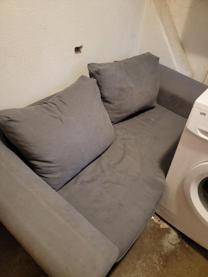Un canapé gris dépliable avec deux gros coussins