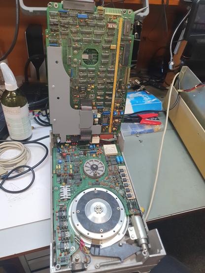 The hard drive unit from the computer. It is an 8 inch model like the tape drive. Two of the PCBs are folded upwards, the remaining two are still attached to the drive. A large hub for the drive mechanism is also visible, as well as the brake pad that holds the platters still while the drive is turned off.