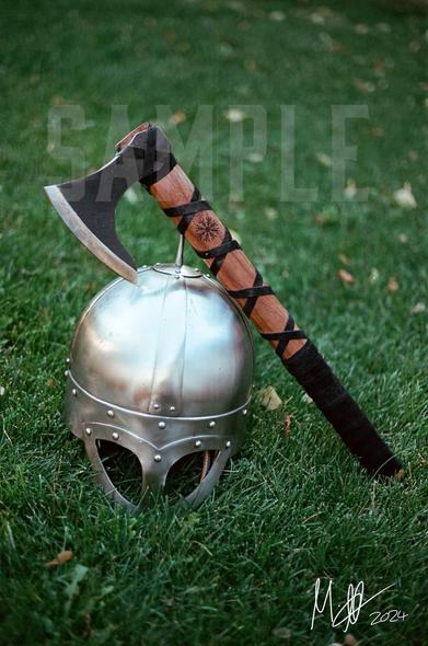 A photograph, shot by Mark, on re-spooled aerial surveillance film depicting a Viking helmet sitting in grass as a bearded axe leans up on it