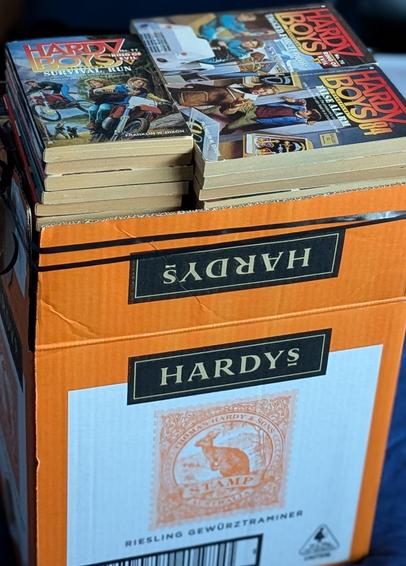 A cardboard wine box stuffed with Hardy Boys books.
The box is labelled Hardys Riesling Gewurztraminer.